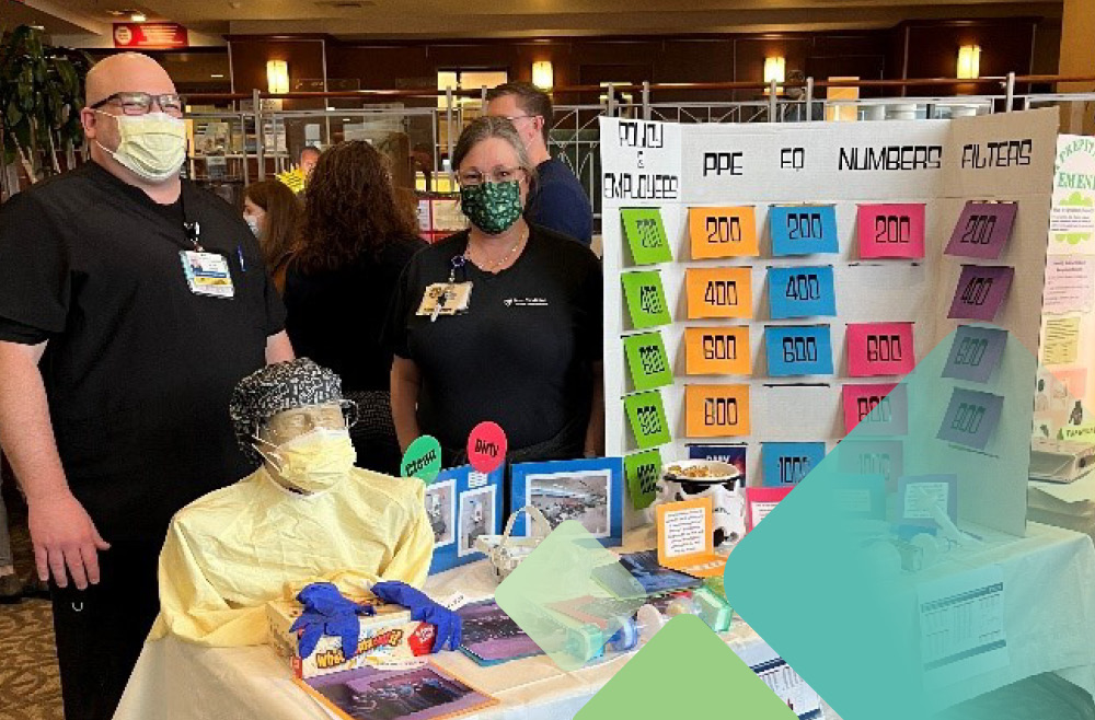 Two respiratory therapists with a trifold tabletop poster set up like a quiz-show game 